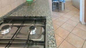 Eine Küche mit einem Gaskochfeld, einer grünen Schüssel und einem Essbereich mit Tisch und Stühlen.