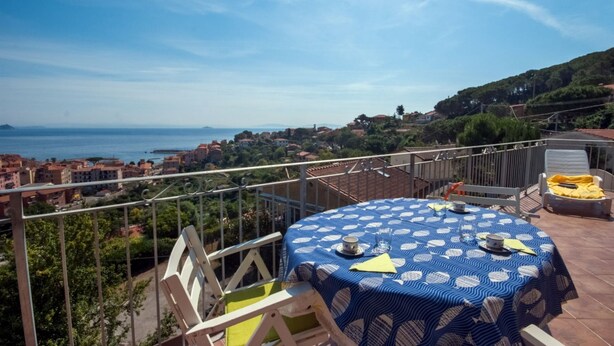 Une terrasse avec une table dressée pour deux personnes, offrant une vue sur une ville côtière et la mer.