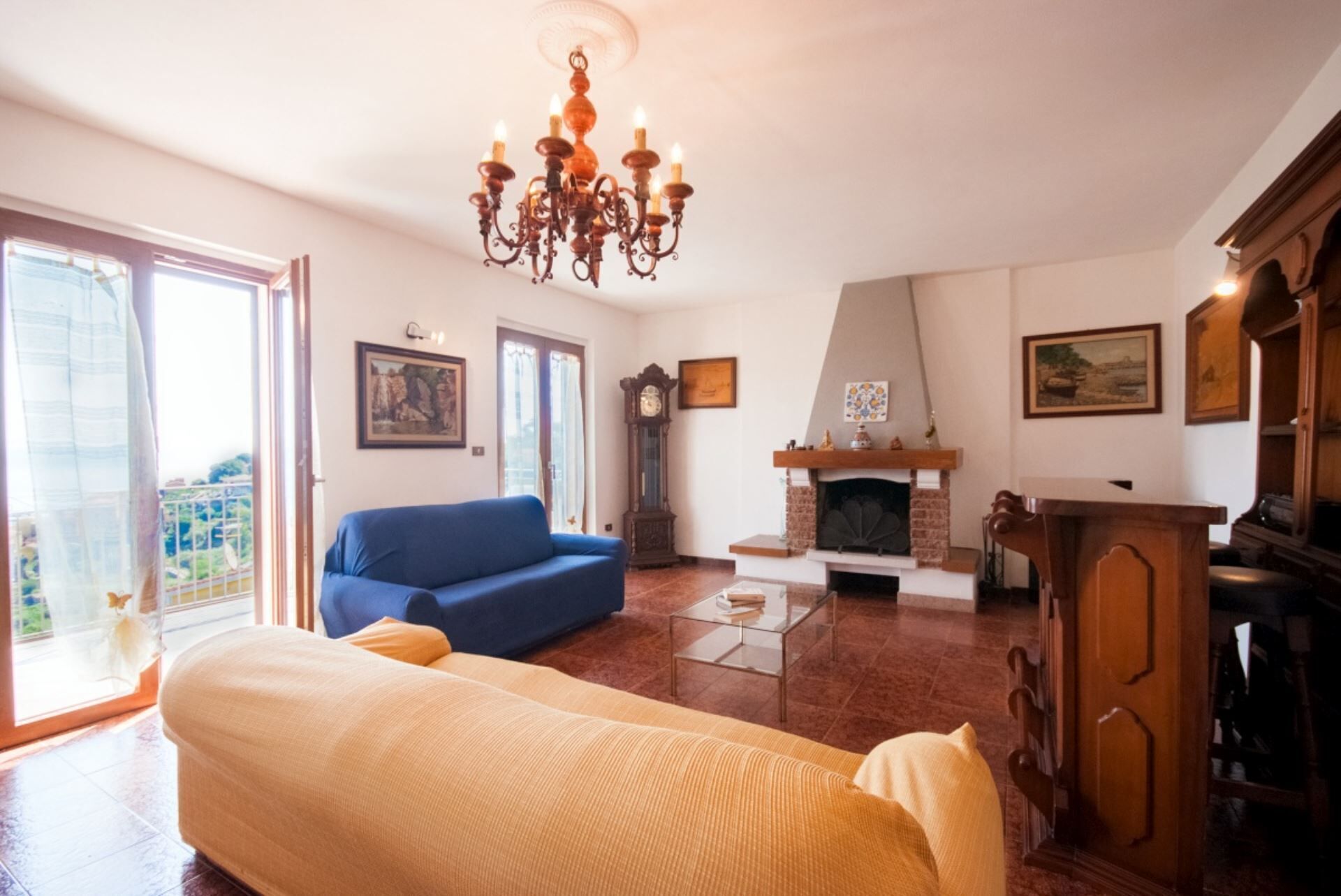 A living room with a blue sofa, a yellow sofa, a fireplace, a wooden cabinet, and a chandelier.