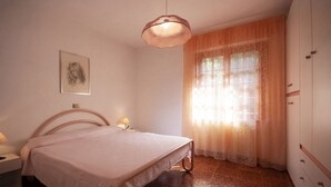 Une chambre à coucher avec un lit, une table de chevet, une lampe, une armoire et une fenêtre avec des rideaux.