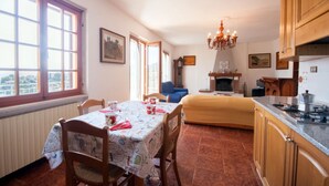 Un coin repas chaleureux avec une table dressée pour deux personnes, un canapé bleu, une cheminée et une cuisine dotée de meubles en bois et d’une cuisinière.