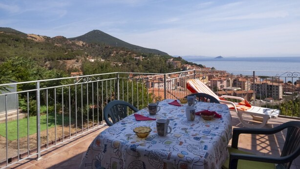 A balcony with a table set for dining, overlooking a coastal town and the sea. - Three-room apartment Villa Paola in Rio Marina (Rio Marina)