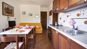 A compact kitchen with wooden cabinets, a stainless steel sink, and a dining area with a table set for two. - Three-room apartment Villa Paola in Rio Marina (Rio Marina)