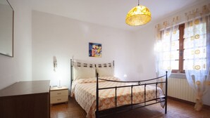 A bedroom with a bed, bedside table, lamp, and a painting on the wall. - Four-room apartment  with a view over Rio Marina (Rio Marina)