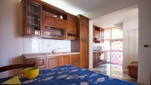 A compact kitchen with wooden cabinets, a countertop, and a window with floral curtains. - Four-room apartment  with a view over Rio Marina (Rio Marina)