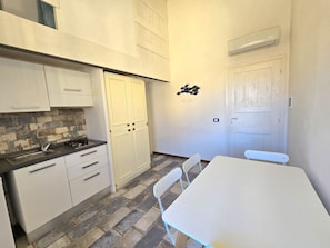 A compact kitchen with white cabinets, a tiled backsplash, a gas stove, and a small dining table with chairs.