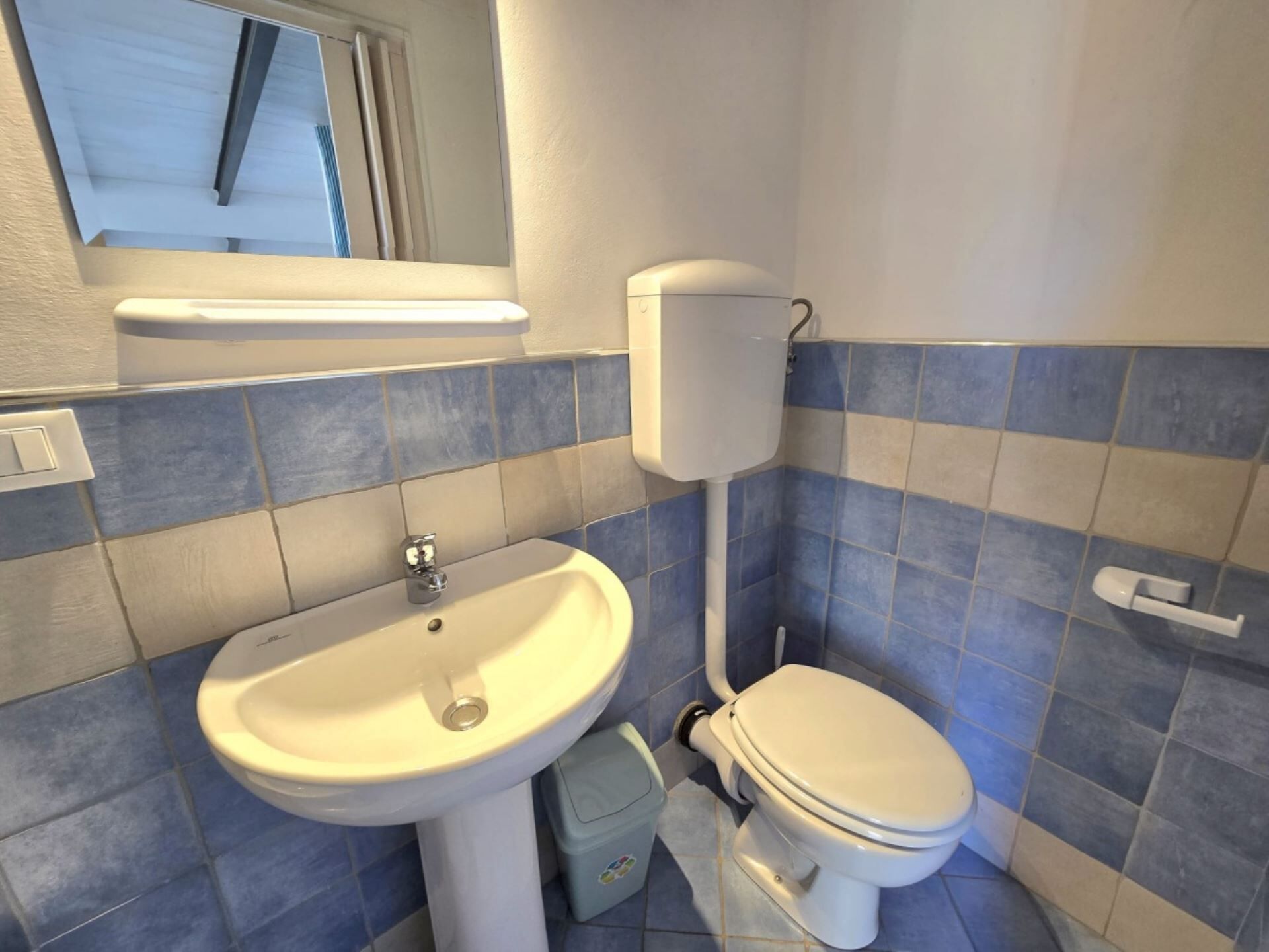 A bathroom with a sink, toilet, and blue-tiled walls.