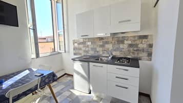 Una cucina compatta con pensili bianchi, zoccolo in piastrelle e una finestra che lascia entrare luce naturale.