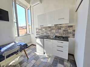 Cozinha compacta com armários brancos, painel de azulejos e uma janela que traz luz natural.