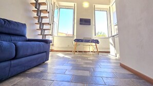 Una habitación con un sofá azul, una mesa pequeña con mantel estampado y una escalera que sube a un nivel superior.