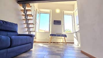 Ein Zimmer mit einem blauen Sofa, einem kleinen Tisch mit gemustertem Tischläufer und einer Treppe, die zu einer oberen Ebene führt.