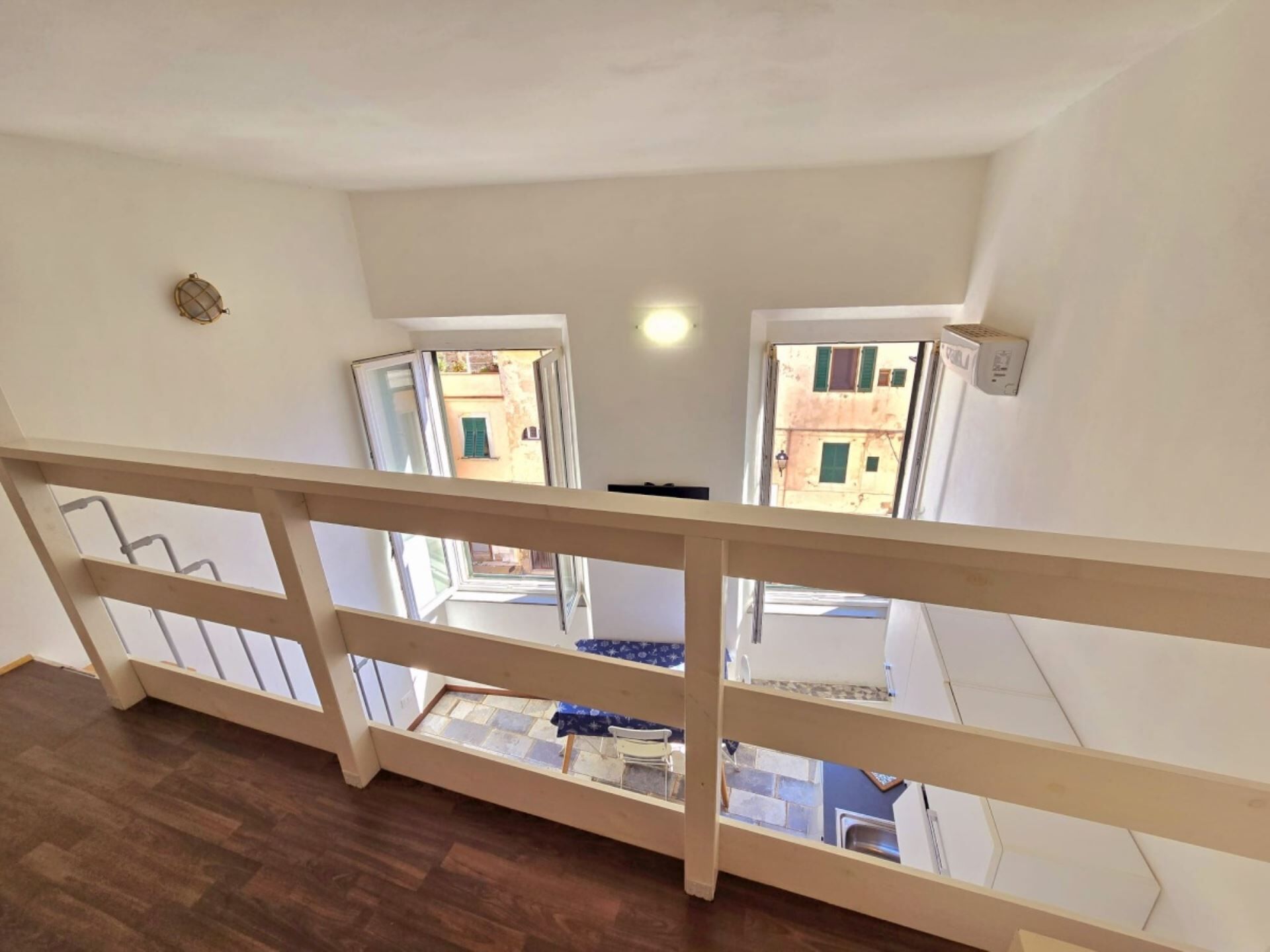 Vista da un balcone con ringhiera in legno, che si affaccia su un pavimento piastrellato e un tavolino con una sedia.