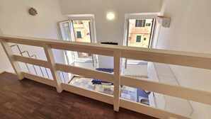Vista desde un balcón con baranda de madera, que da hacia un suelo de baldosas y una pequeña mesa con una silla.