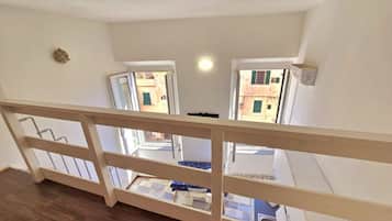 Vista da un balcone con ringhiera in legno, che si affaccia su un pavimento piastrellato e un tavolino con una sedia.