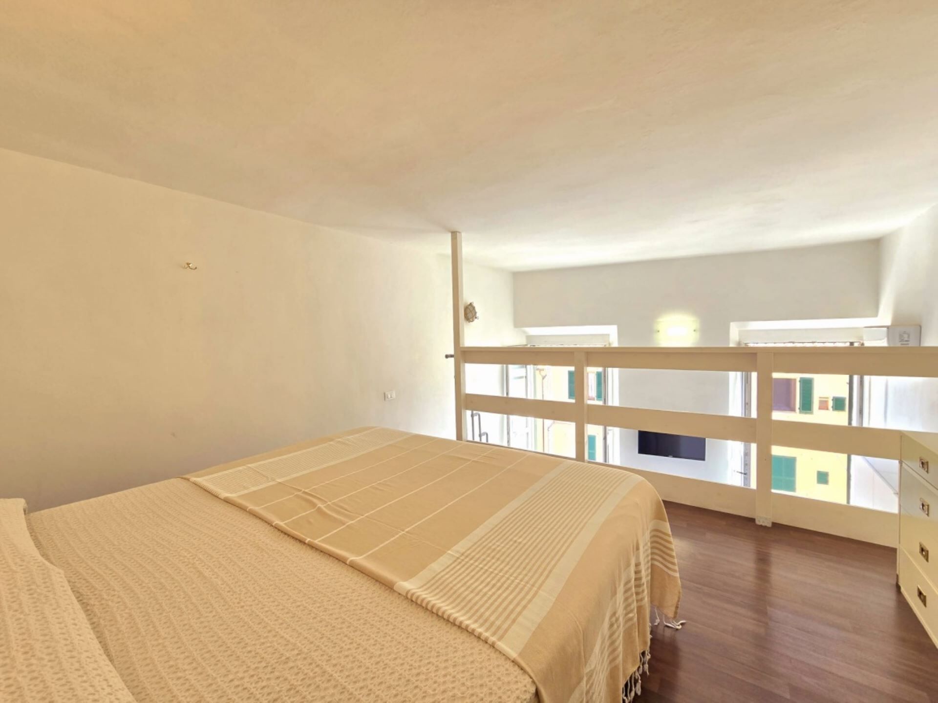 A bedroom with a bed, a balcony with a railing, and a view of buildings outside.