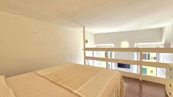 A bedroom with a bed, a balcony with a railing, and a view of buildings outside.
