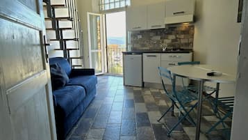 A compact kitchen with a dining area, a sofa, and a view through an open door.