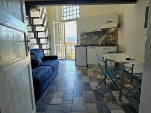 Uma cozinha compacta com área de refeições, um sofá e vista através de uma porta aberta.