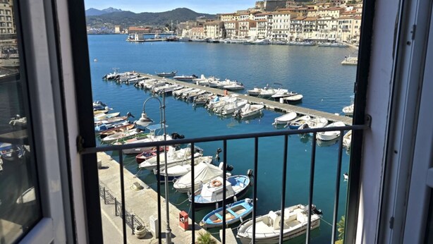 A marina with boats docked, a clear view of the water, and buildings in the background.