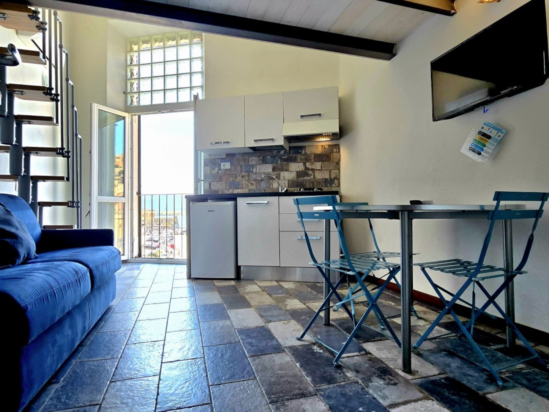 Un angolo cottura compatto con zona pranzo, un divano e vista attraverso una porta vetrata.