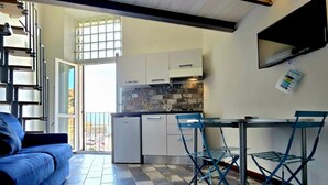 A compact kitchen with a dining area, a sofa, and a view through a glass door.