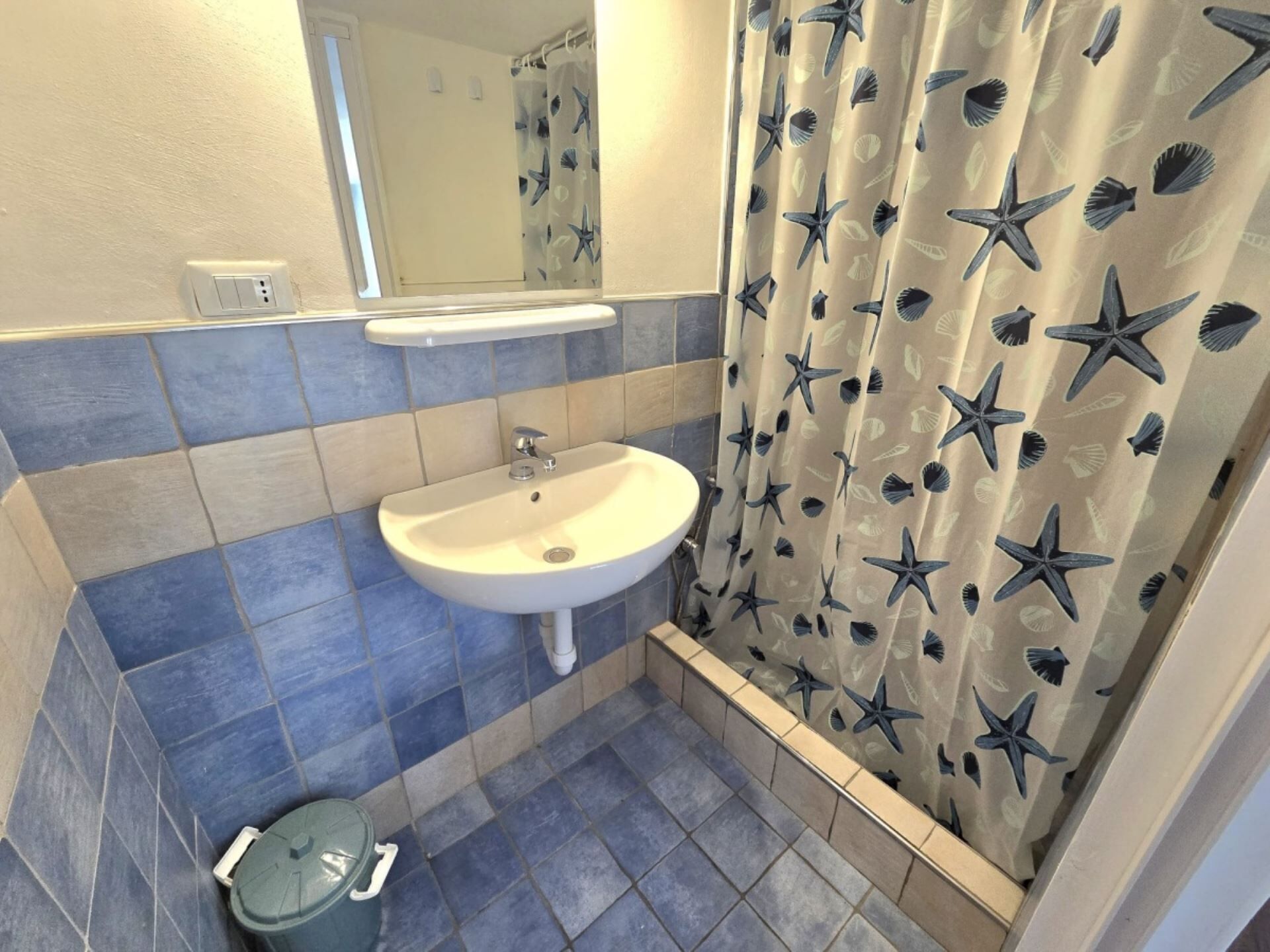 A bathroom with a sink, mirror, and shower curtain with a starfish pattern.