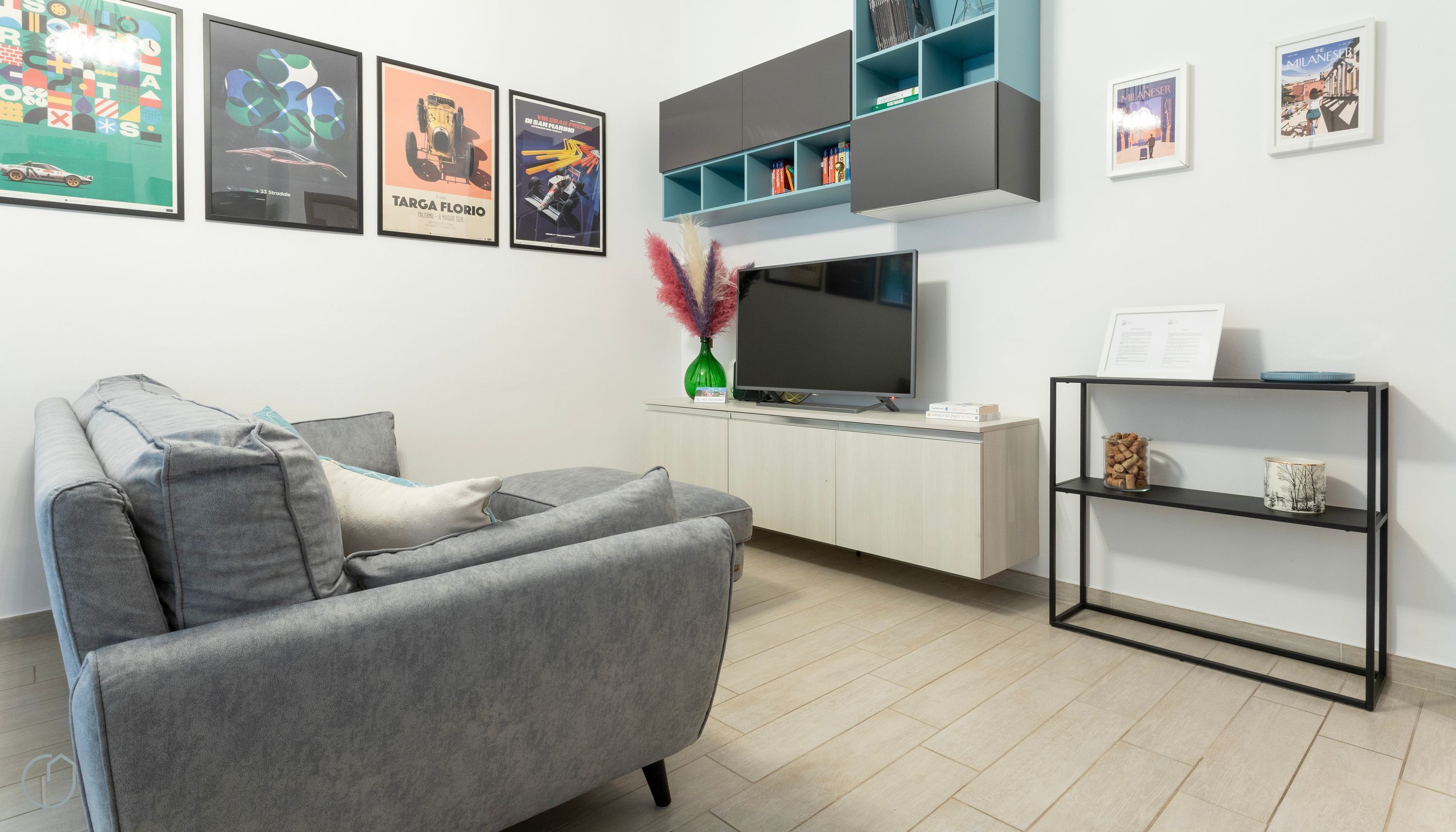 A modern living room with a grey sofa, a flat-screen TV, and a bookshelf.
