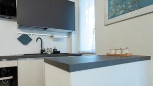 A modern kitchen with a grey countertop, a black faucet, and a window with sheer curtains. - Italianway - Martinetti 19 (Milan)