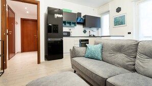 A modern apartment with a grey sofa, a kitchen with a built-in oven, and a wooden door. - Italianway - Martinetti 19 (Milan)