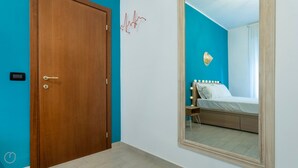 A bedroom with a wooden door, a bed with white bedding, a nightstand, and a mirror with a lighted wall decoration. - Italianway - Martinetti 19 (Milan)
