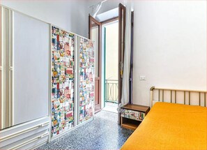 A bedroom with a bed, a wardrobe, a small table, and a balcony door.