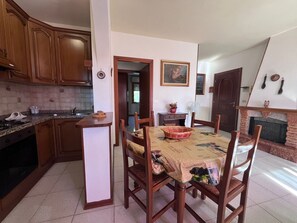 A kitchen with wooden cabinets, a dining table with chairs, a fireplace, and a painting on the wall.