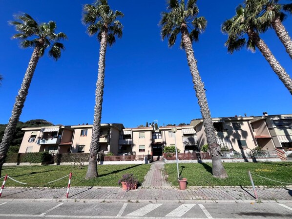 A row of palm trees in front of a row of beige apartment buildings with a clear blue sky.