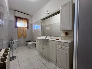 A bathroom with white tiles, a sink, a toilet, and a shower area.