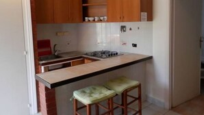 A compact kitchen with wooden cabinets, a gas stove, and two stools.