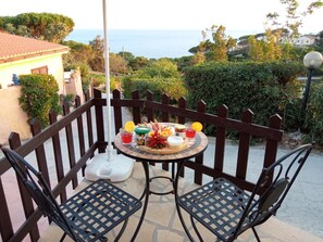 Un patio con un tavolo rotondo apparecchiato per due, circondato da una recinzione di legno, con vista panoramica sul mare e sulle colline.