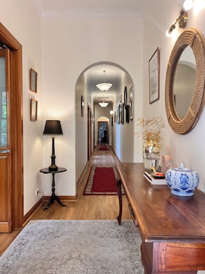 A hallway with a wooden floor, a red carpet, a round mirror, and framed pictures on the walls.