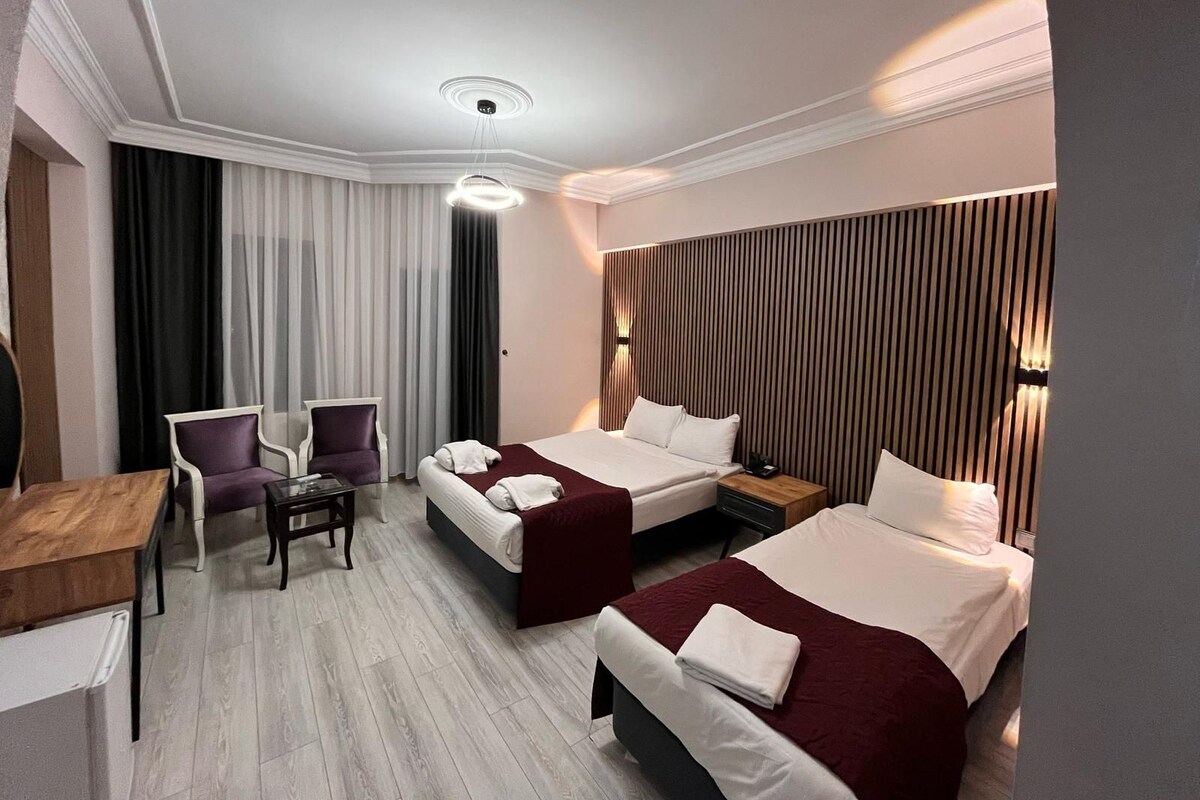 A hotel room with two beds, a desk, a chair, and a wooden panel wall.