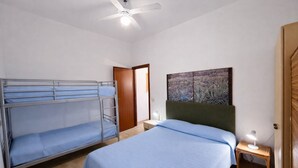 Un dormitorio con literas, una cama individual, ventilador de techo, mesita de noche con lámpara y una puerta.