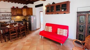 A cozy kitchen with wooden cabinets, a red sofa, and a dining area with a table and chairs. - La Casina Riese in the heart of Rio nell'Elba (Rio dell'Elba)