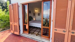 A bedroom with a bed, a nightstand, and a window overlooking a garden.