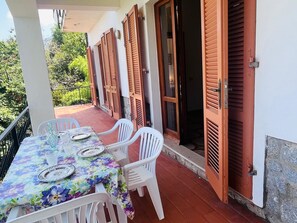 Un balcón con una mesa lista para dos personas, sillas de plástico blanco y contraventanas de madera en las paredes.