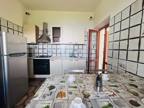 Cozinha equipada com geladeira, fogão, pia e armários. Há uma mesa de jantar com um jogo americano com ilustrações de comida.