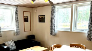 A room with a wooden ceiling, a sofa, a table with chairs, and two windows with curtains. - Sölvesborgs Golfklubb (Sölvesborg)