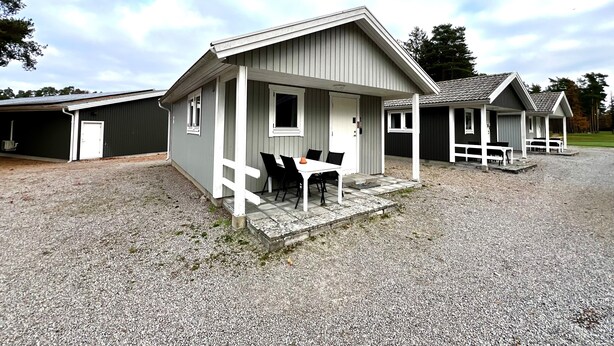 A row of small, single-story cabins with a gravel driveway and a covered outdoor seating area. - Sölvesborgs Golfklubb (Sölvesborg)