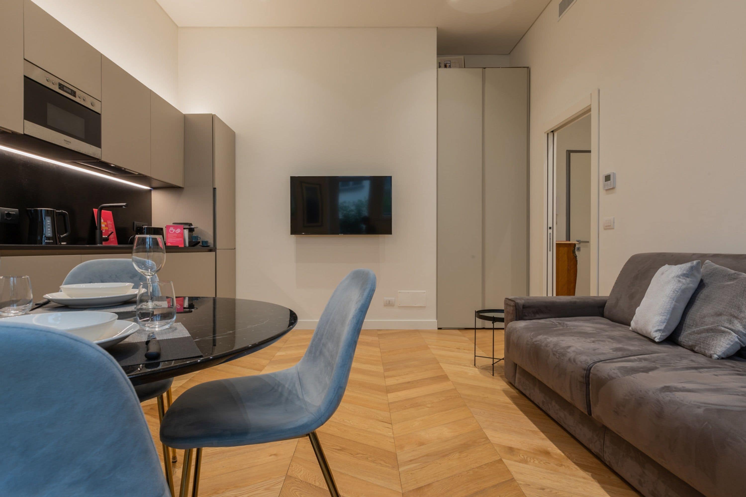 Una cocina moderna con comedor, un televisor de pantalla plana en la pared y un sofá gris en la sala.