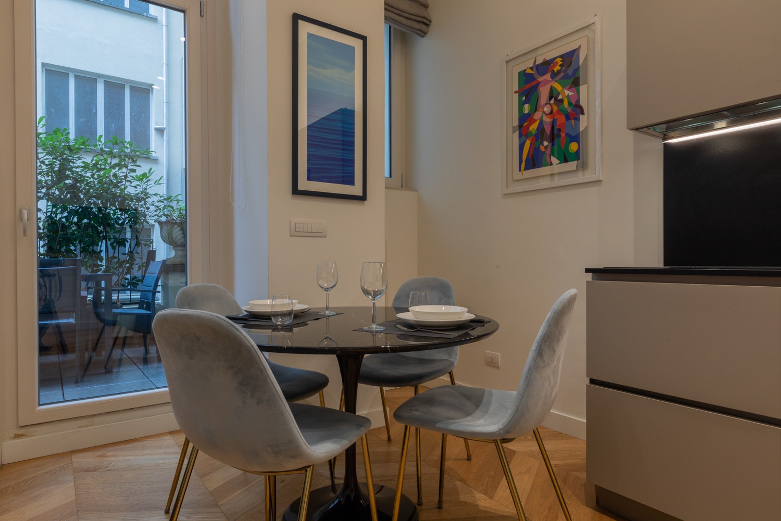 A dining area with a table set for two, two chairs, and a modern kitchen with a refrigerator.