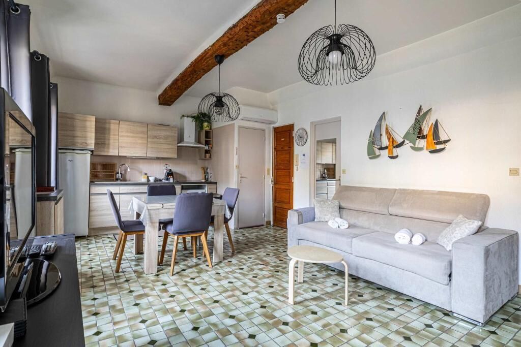 A modern kitchen with wooden cabinets, a dining area with a table and chairs, a grey sofa, and decorative sailboat wall art.