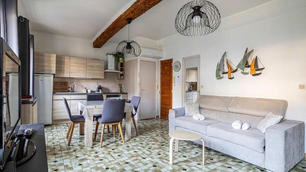 Une cuisine moderne avec des meubles en bois, un coin repas comprenant une table et des chaises, un canapé gris et des œuvres d’art décoratives représentant des voiliers.
