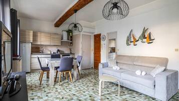 A modern kitchen with wooden cabinets, a dining area with a table and chairs, a grey sofa, and decorative sailboat wall art.